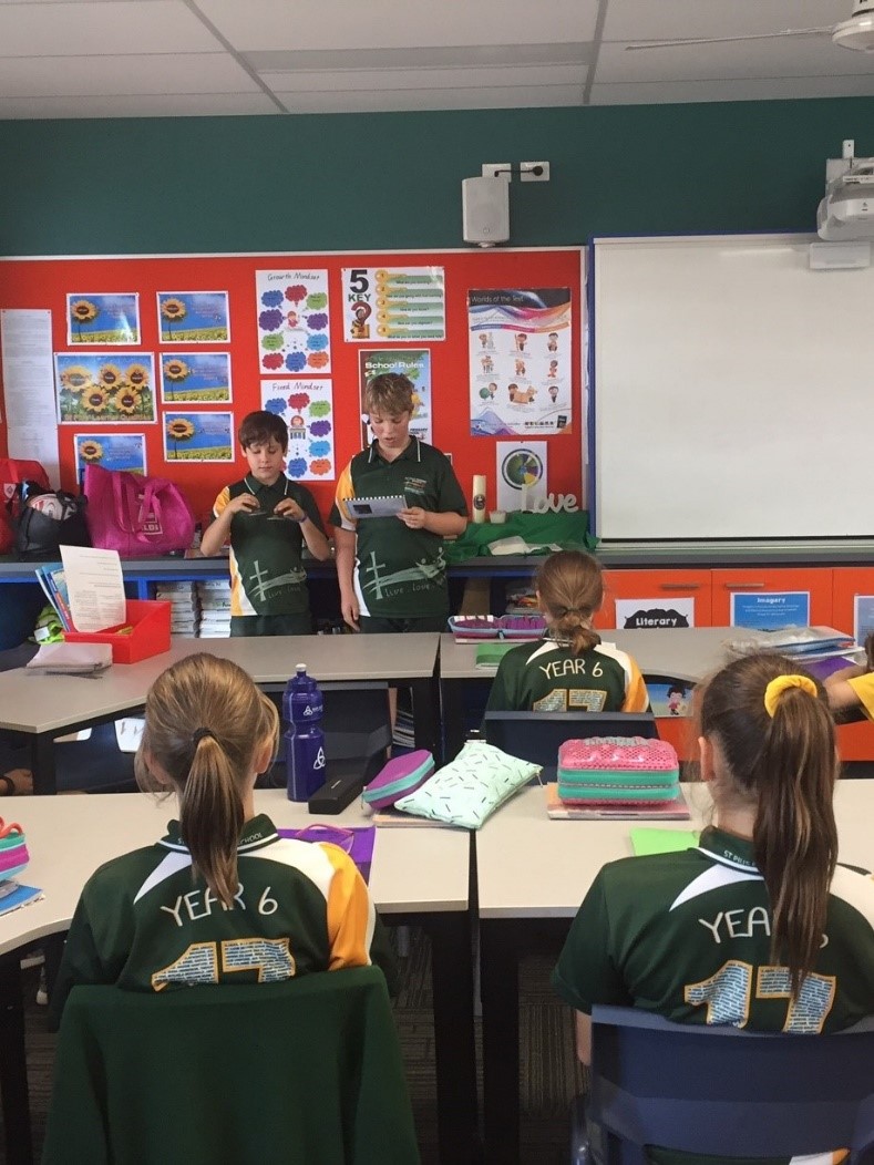 Students seated in a classroom while two students stand at the front presenting to the class