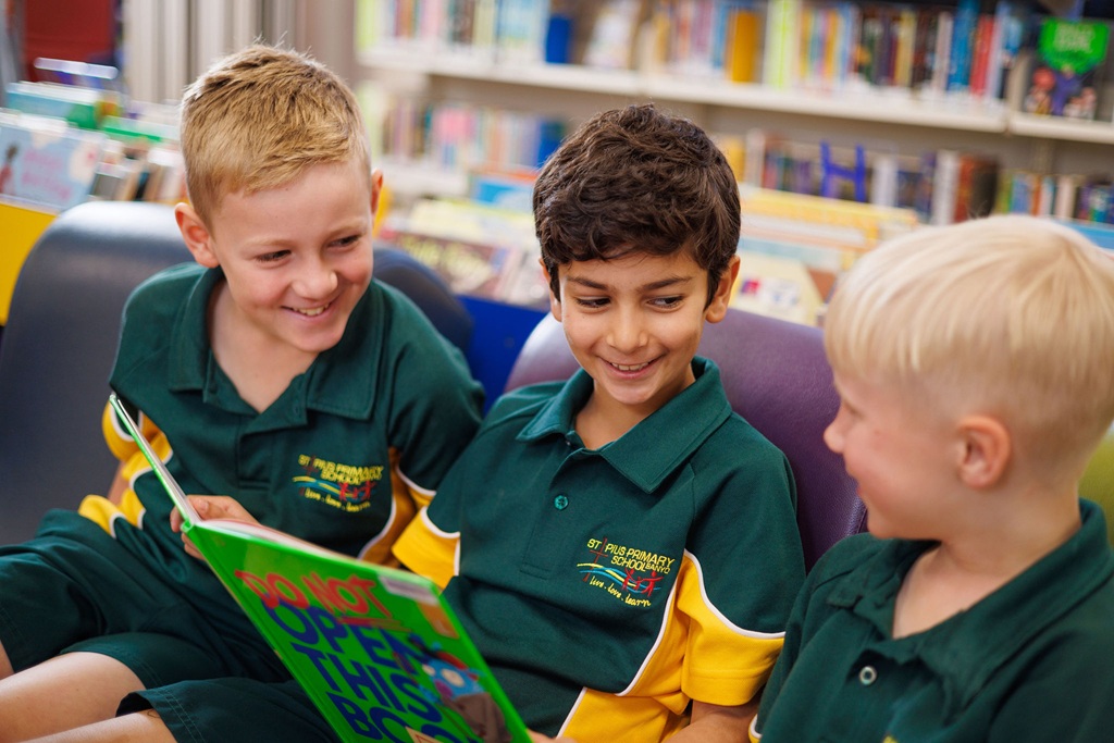 Three students sitting together in a library reading a book