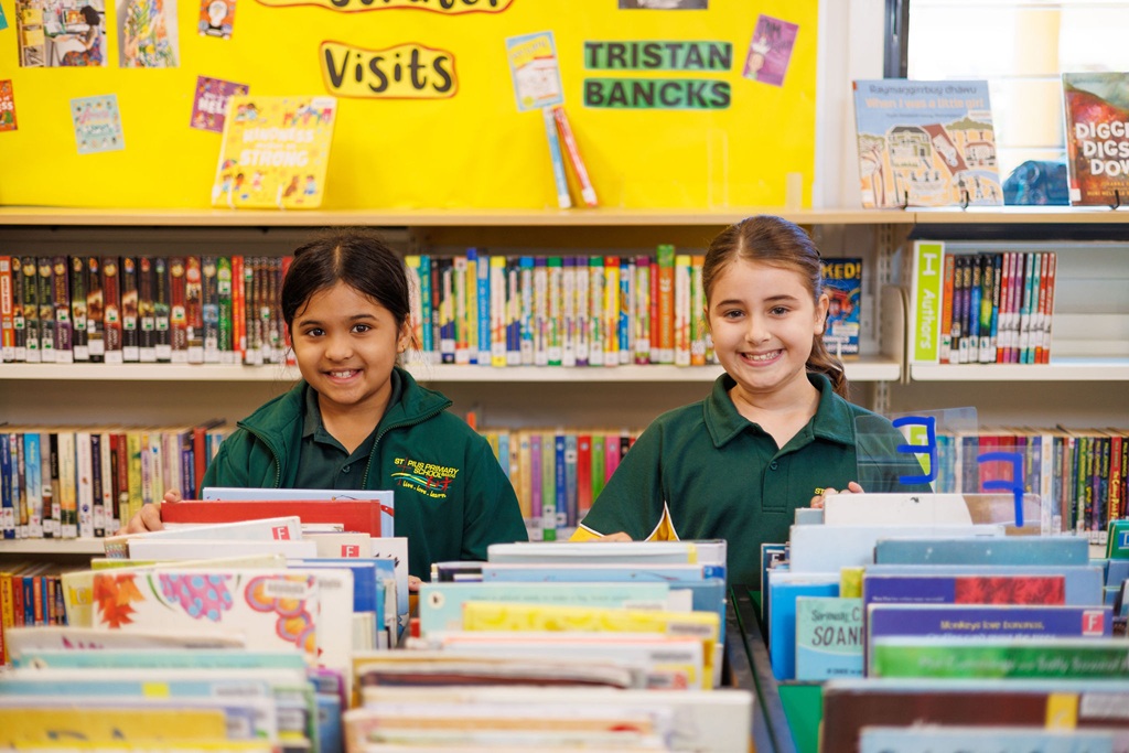 Two students standing behind a table of books in a school library