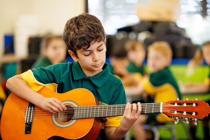 Student in school uniform playing an acoustic guitar during a classroom music lesson