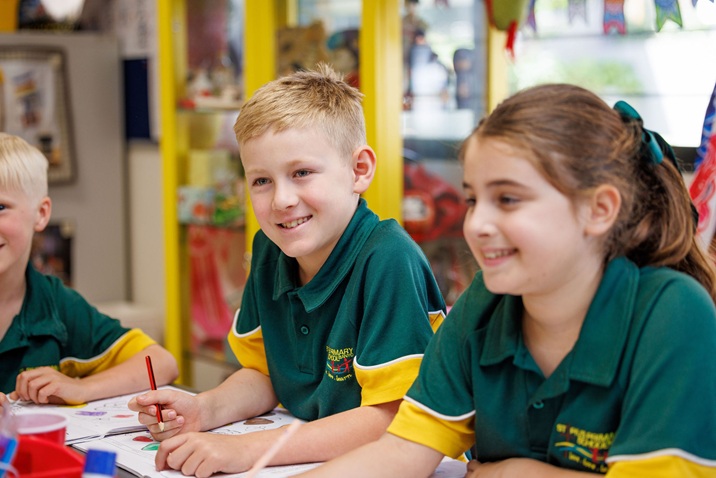 Students in school uniforms sitting at a table drawing and writing together in a classroom