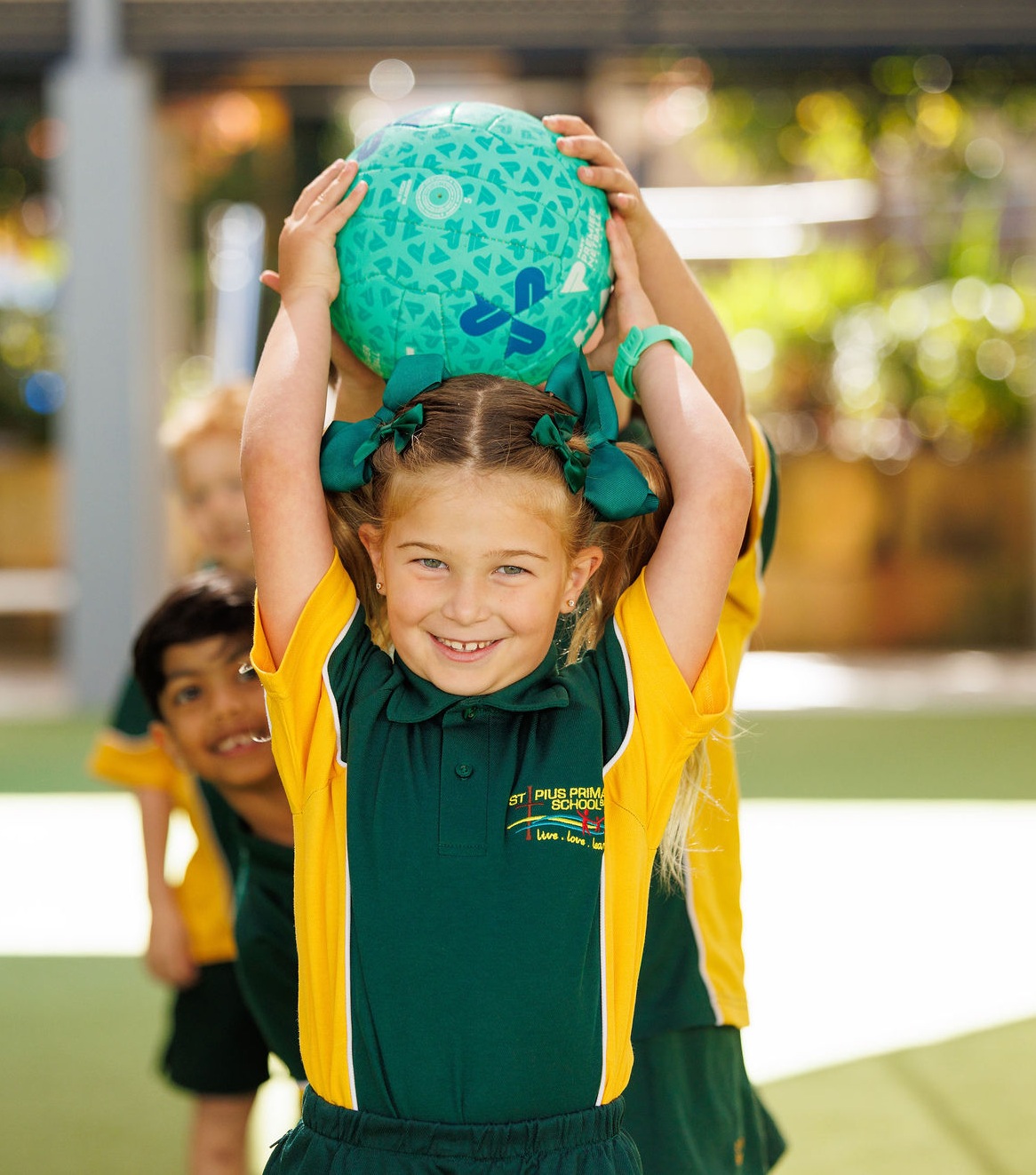 Student in school uniform holding a ball above their head during an outdoor activity