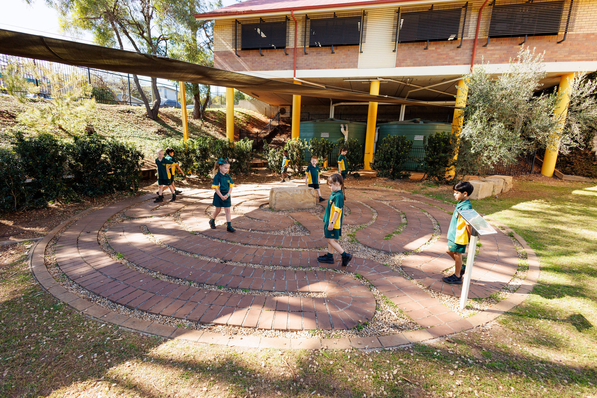 Students in school uniforms walking along a circular brick path in an outdoor learning area