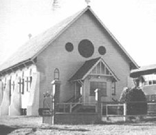 Historic black and white photograph of a church building with a gabled roof and circular windows near the entrance
